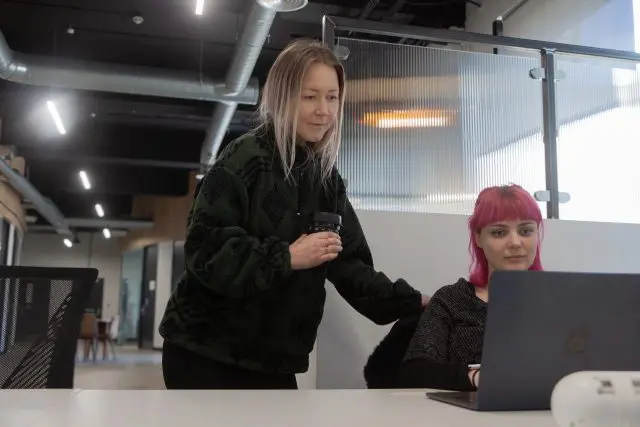 Two female team members working, both looking at a laptop screen