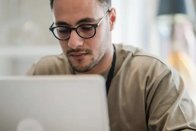 Man wearing glasses looking down at and working on his laptop